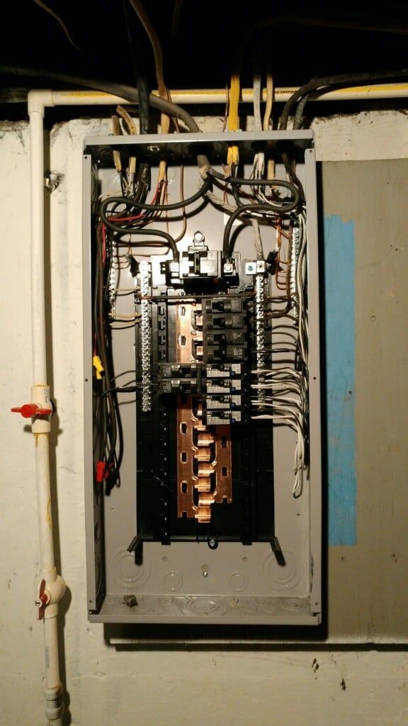 A electrical panel is hanging on a wall in a basement.