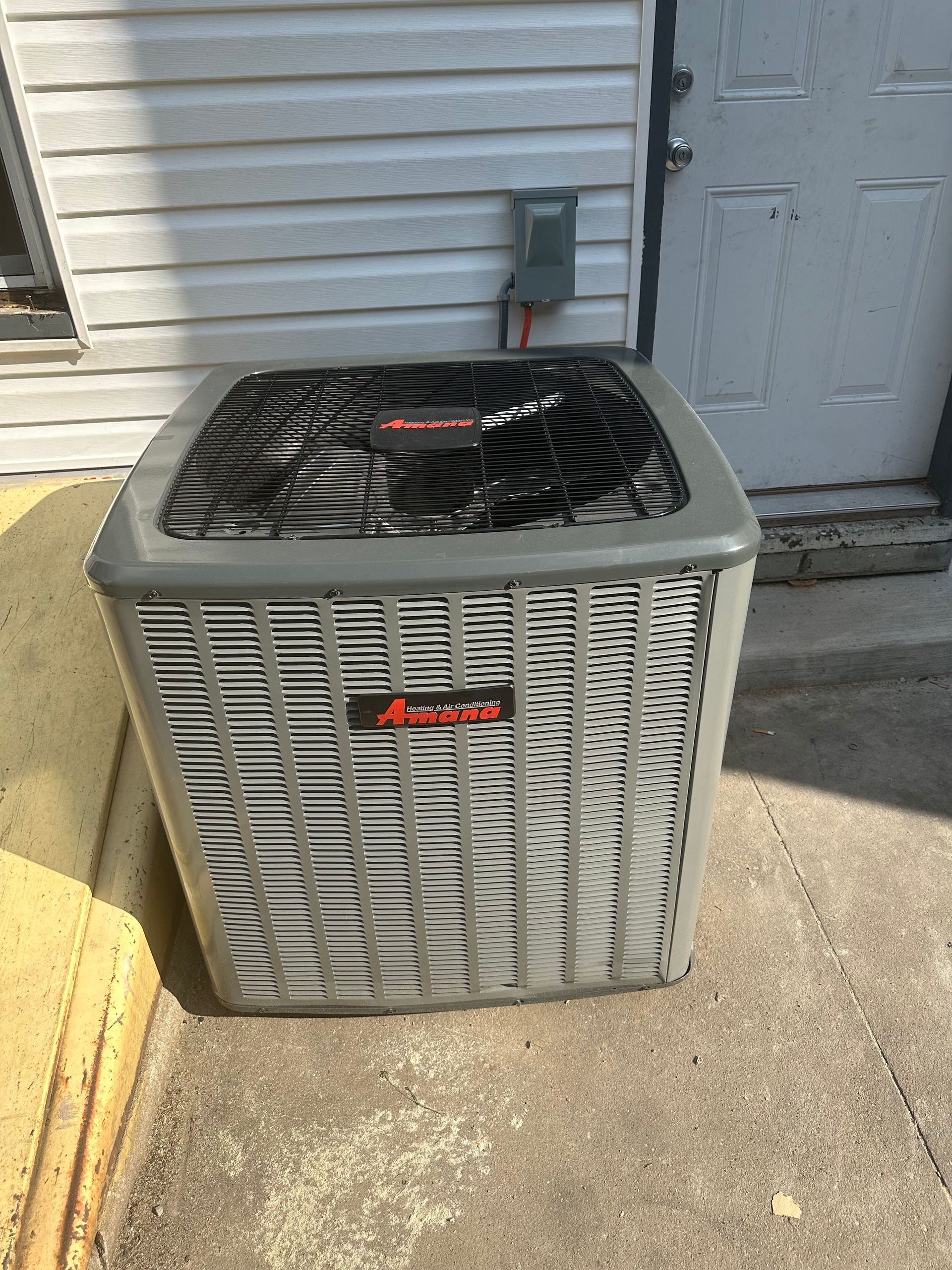 An air conditioner is sitting on the sidewalk in front of a house.