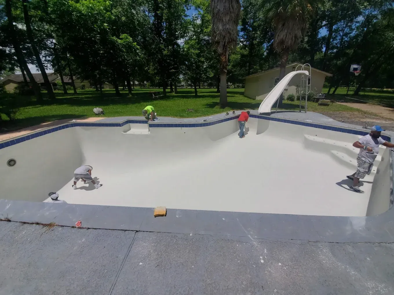 A man is working on a swimming pool with a slide in the background.