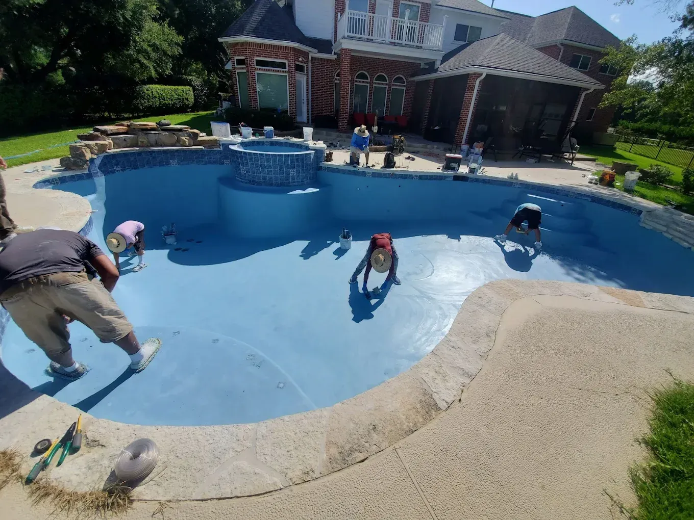 A group of people are working on a swimming pool in front of a large house.