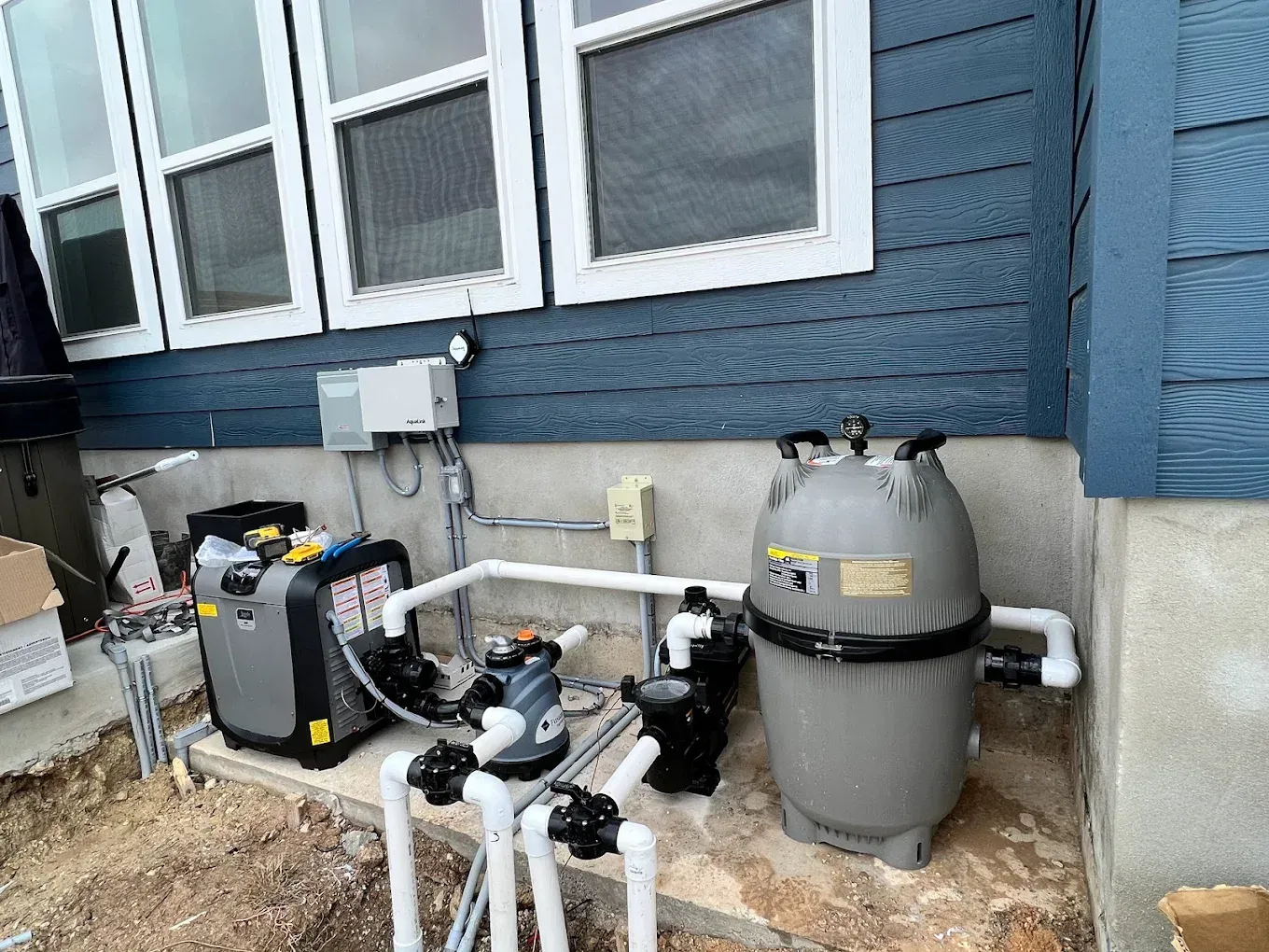 A swimming pool pump and filter are sitting on the side of a house.
