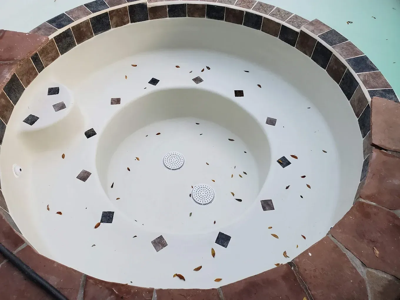 A white hot tub with brown and black tiles around it