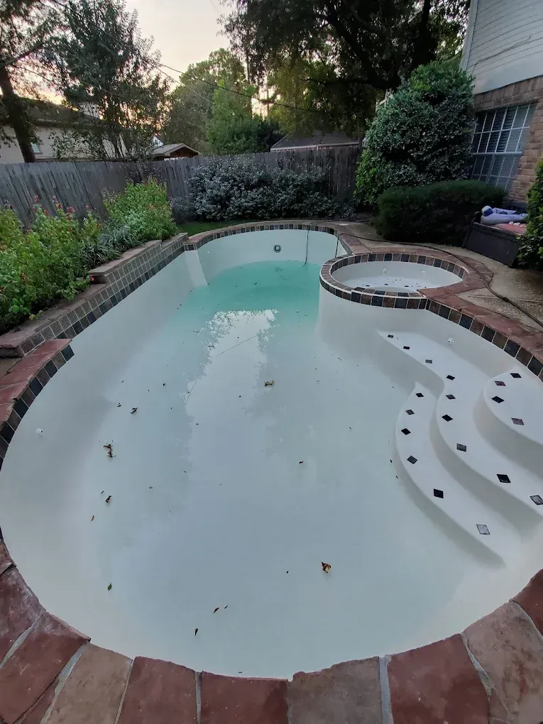 A large swimming pool with steps and a hot tub in the backyard of a house.