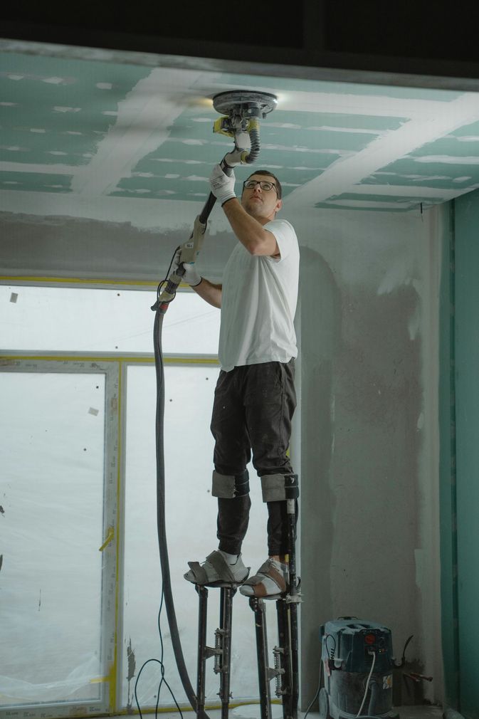 Worker using a drywall sander on a ceiling inside a room under construction