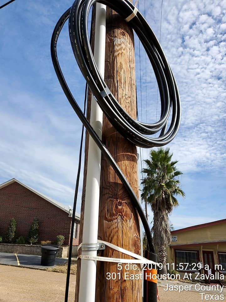 Utility pole with coiled black cable, white conduit, and text in bottom right: