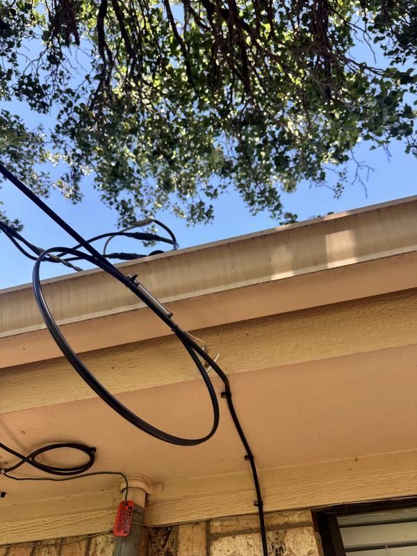 Black cables looped along a beige gutter under a tree, against a blue sky.