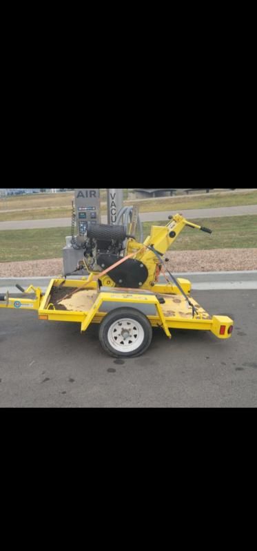 Yellow commercial lawn mower on a trailer, parked on a paved surface.