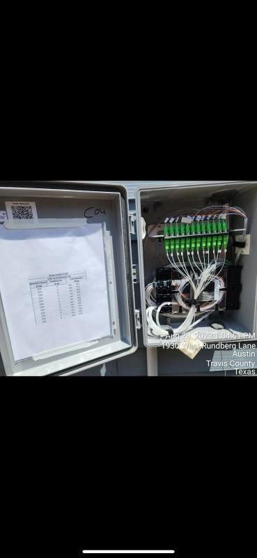 An open gray electrical box with papers and green fiber optic connectors.