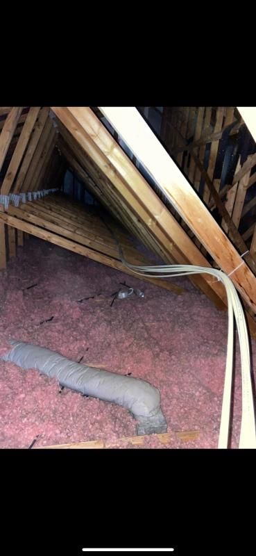 Attic with pink insulation, wooden beams, and a gray vent pipe. White wires are visible.