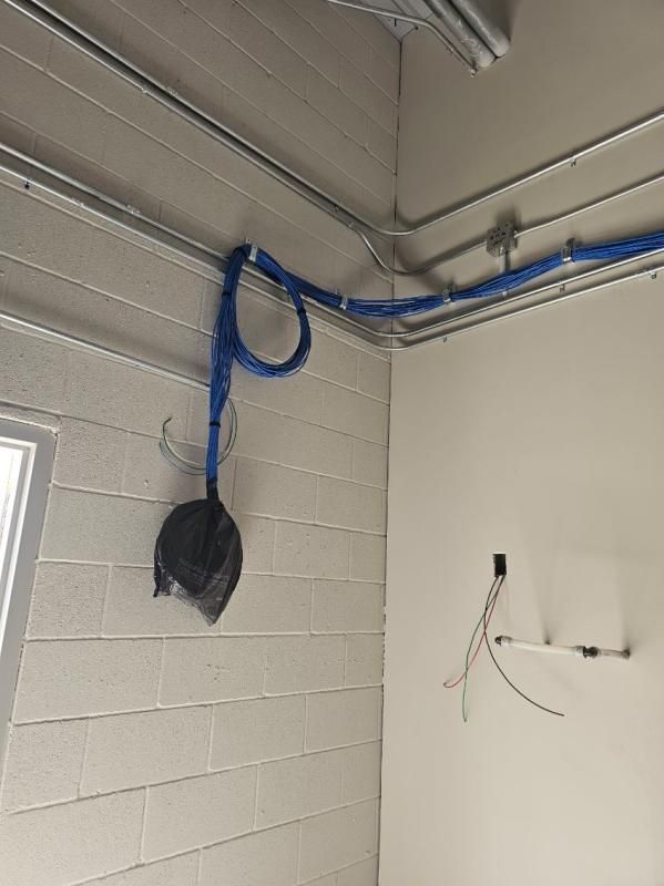 Blue electrical conduit runs along a cinder block wall and ceiling, with a black bag hanging.