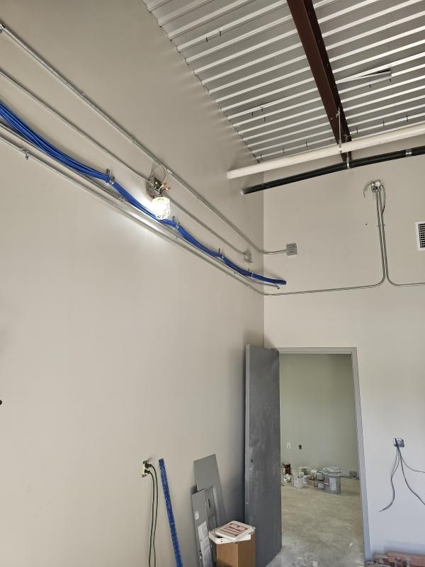 Interior construction scene: exposed wiring, blue cables along a white wall, door, and a partially finished room.