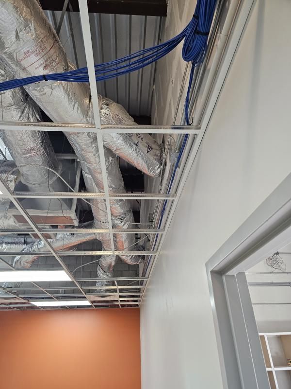 Overhead view of an unfinished ceiling, showing HVAC ducts, wiring, and a drop ceiling grid.