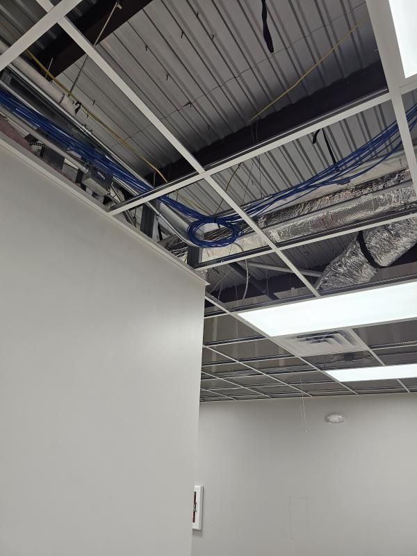 A partial view of an office interior with exposed ceiling grid, wires, and ductwork above a wall.