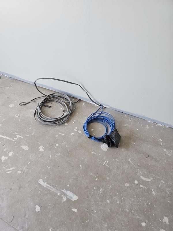Two coiled cables, gray and blue, sit on a concrete floor next to a white wall.