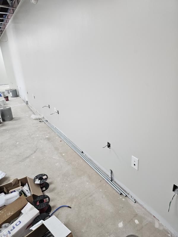 Construction site: White painted wall with exposed electrical conduits and outlets along the floor. Gray concrete floor.