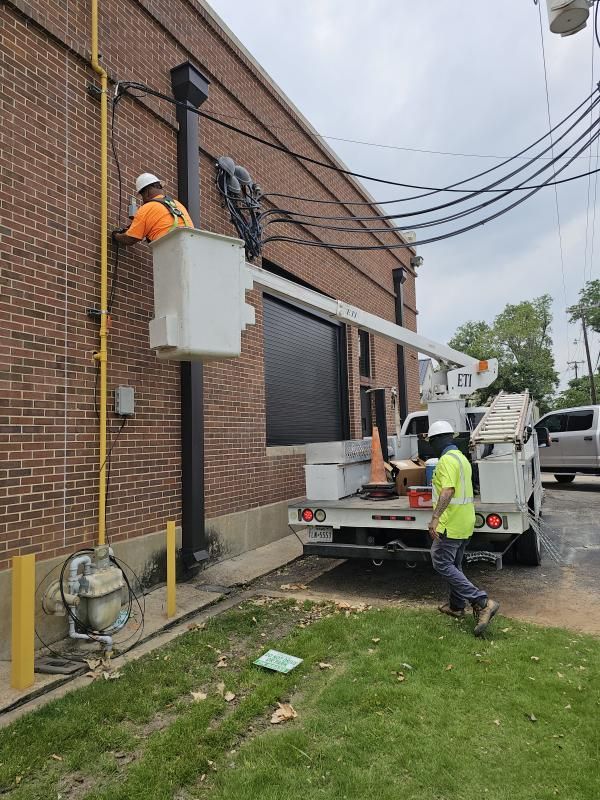 Two utility workers on a lift repairing electrical lines attached to a brick building.