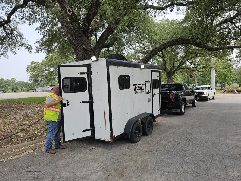 A person in a safety vest opens a white trailer door hitched to a black truck.