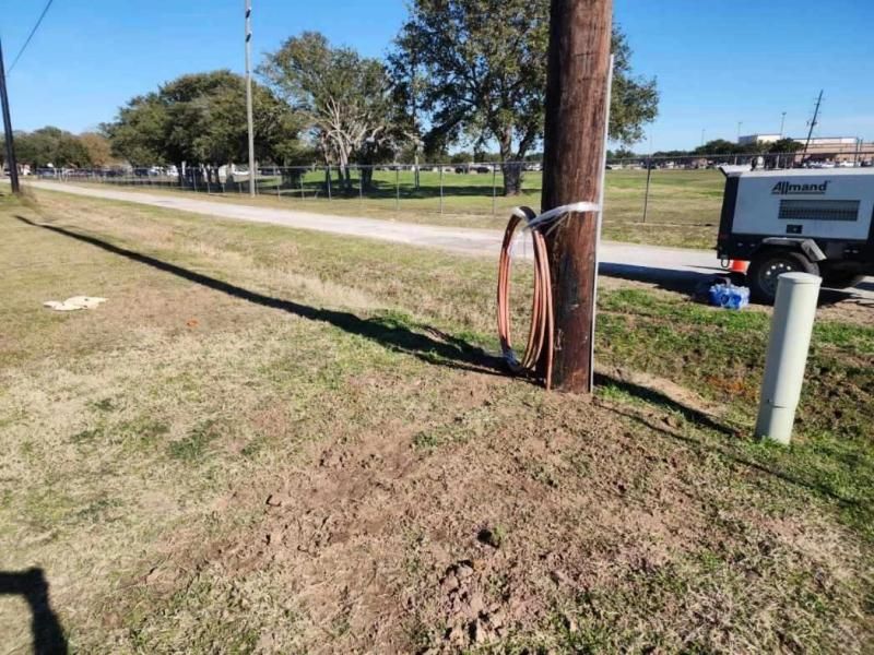 Wooden utility pole with coiled cables secured by tape near a road and grassy area.