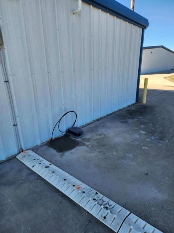 Gray metal building with a black box on the ground, a gray ramp, and a black cable.