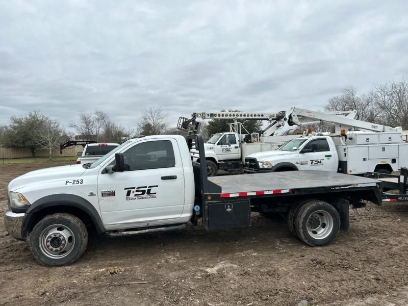 White TSC work truck with flatbed, parked outdoors. Other work trucks with cranes visible.
