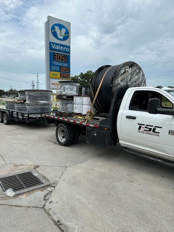 A white pickup truck with a flatbed trailer hauls materials near a Valero gas station.