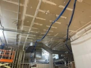 Ceiling construction: drywall grid, blue wires, HVAC ductwork, unfinished room.