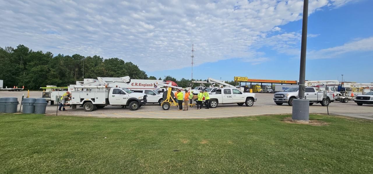 Utility workers and trucks parked outdoors, some workers wearing safety vests.