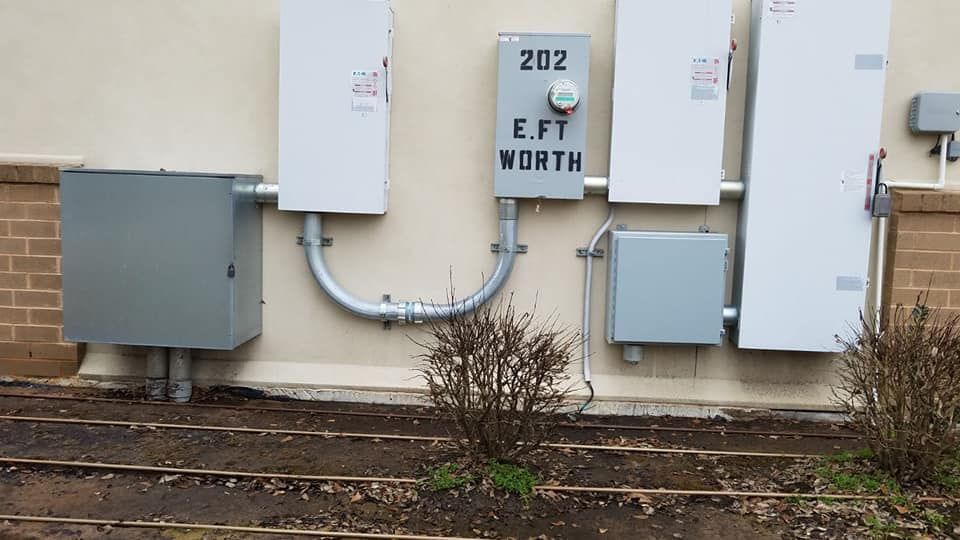 Electrical equipment mounted on a beige wall: boxes, conduits, and a meter labeled 