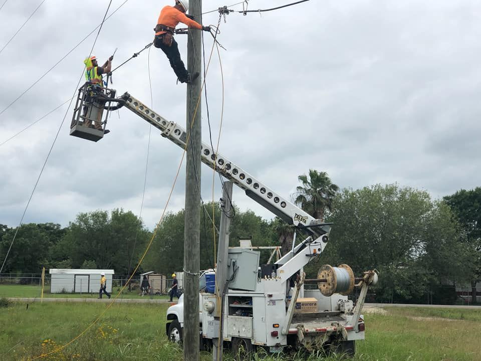 Linemen on a utility pole, one in a lift bucket, others working on power lines, cloudy sky.