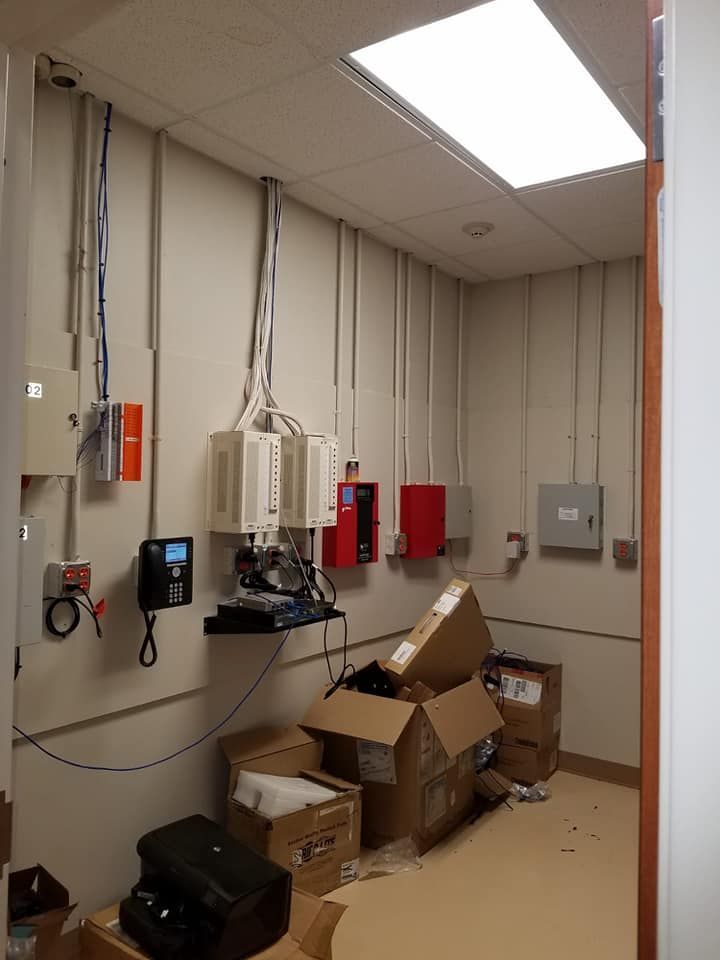 A small utility room with electrical equipment mounted on walls, cardboard boxes, and cables.