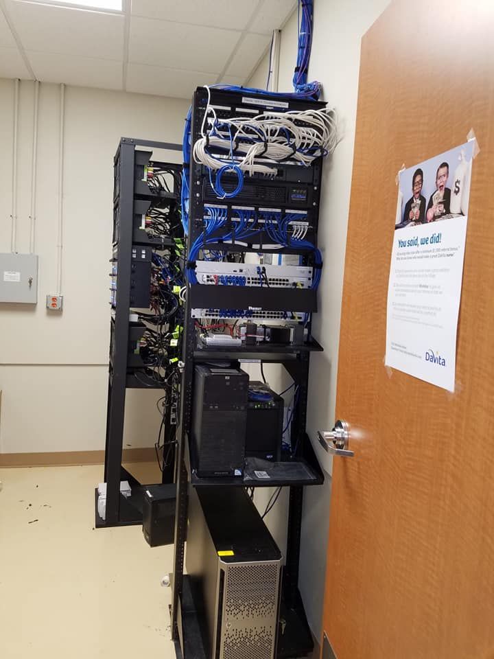 Server racks in a room with network cables, servers, and a door on the right. Blue and white cables are prominent.