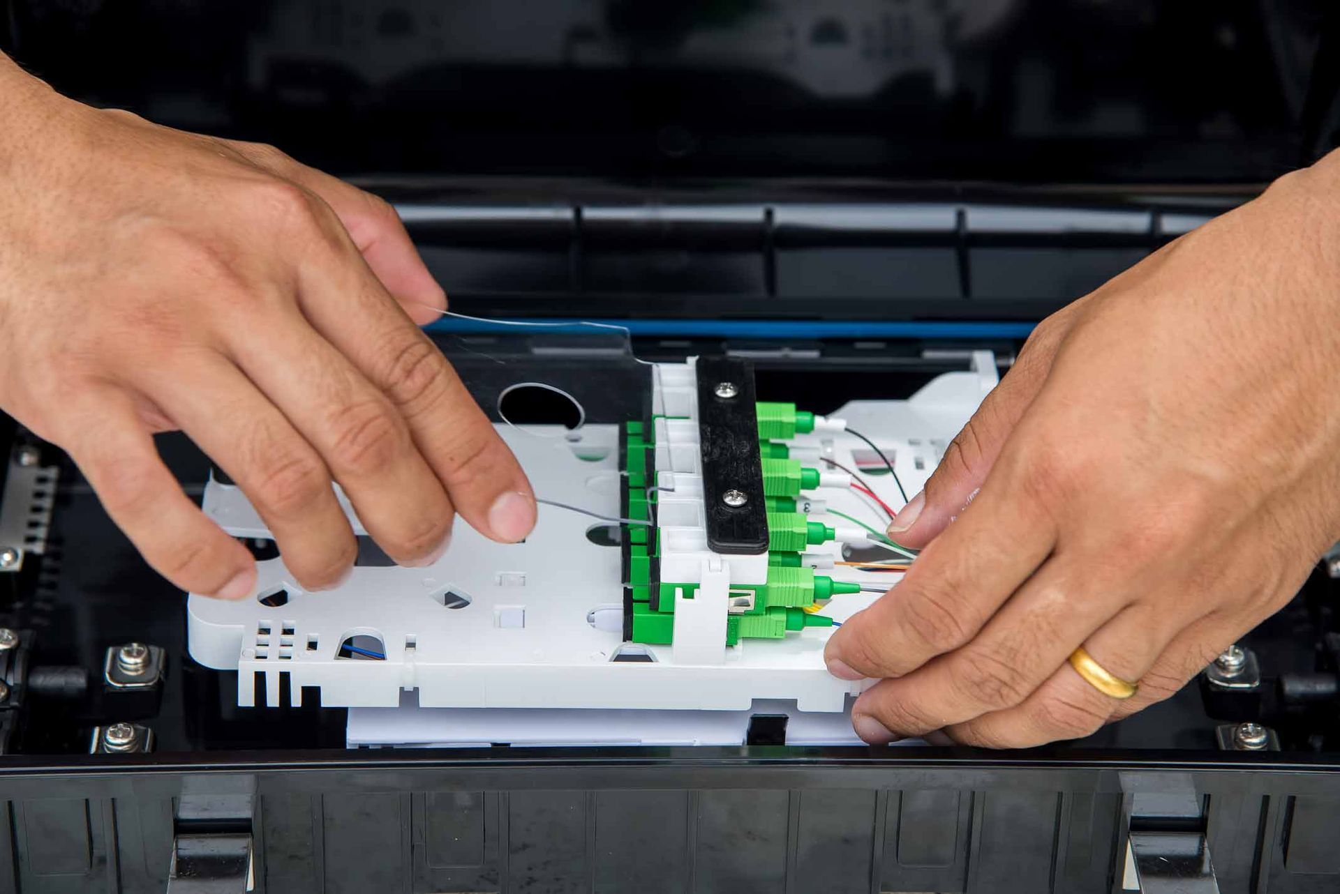 Hands installing fiber optic cables into a black device with green and white components.