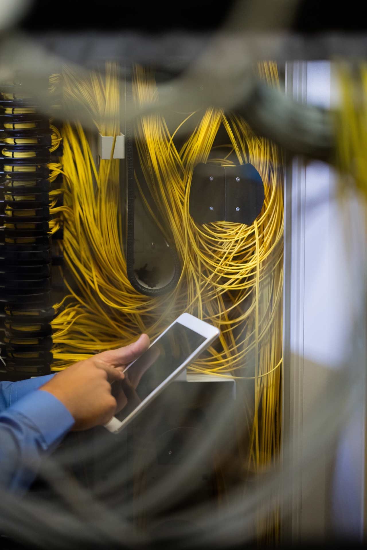 Person using a tablet in front of a server rack with yellow cables.