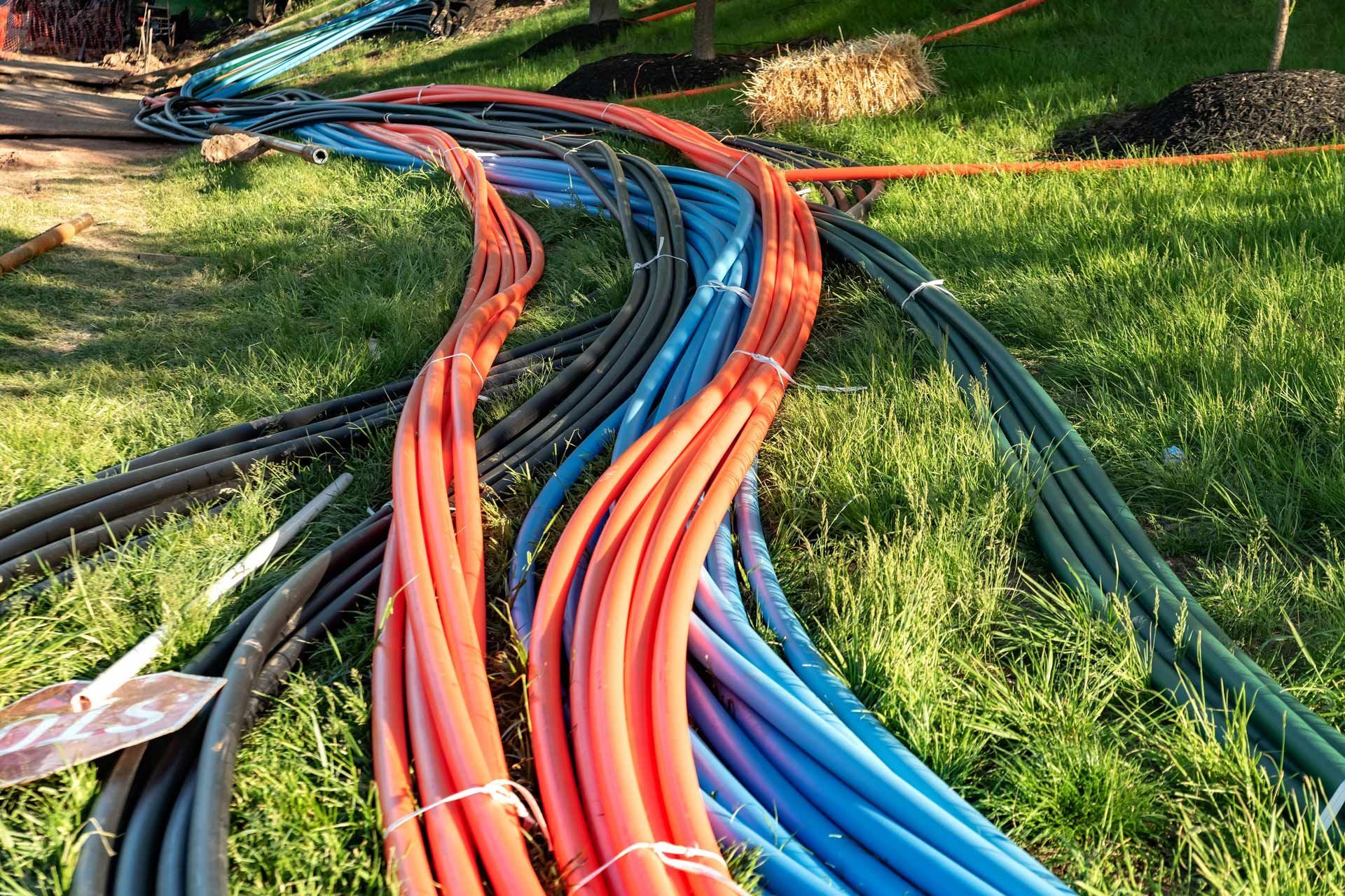 Bundles of colorful electrical conduit tubing spread across a grassy area.