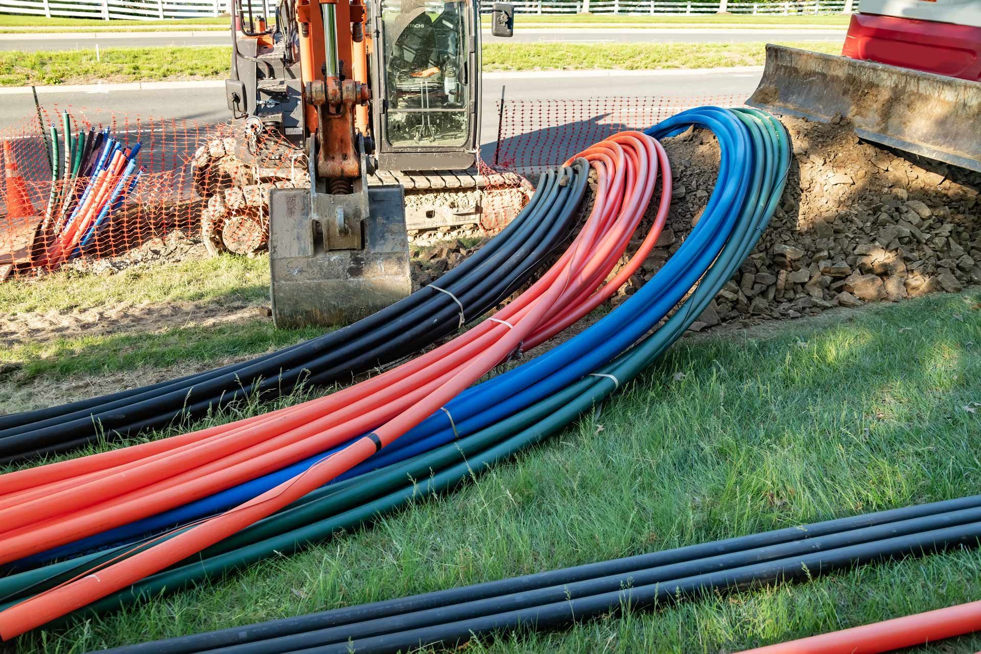 Orange excavator near a ditch with bundles of colored underground utility cables, ready for installation.