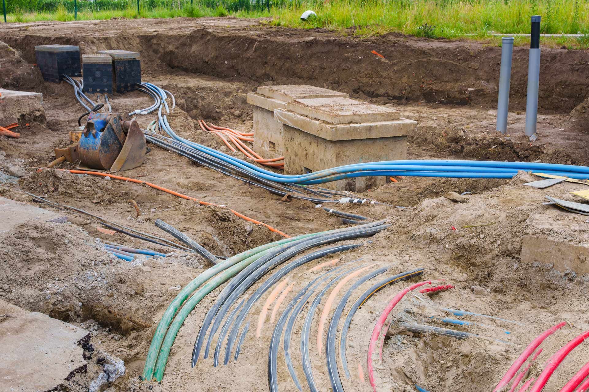 Underground utility cables and boxes in an open trench at a construction site.