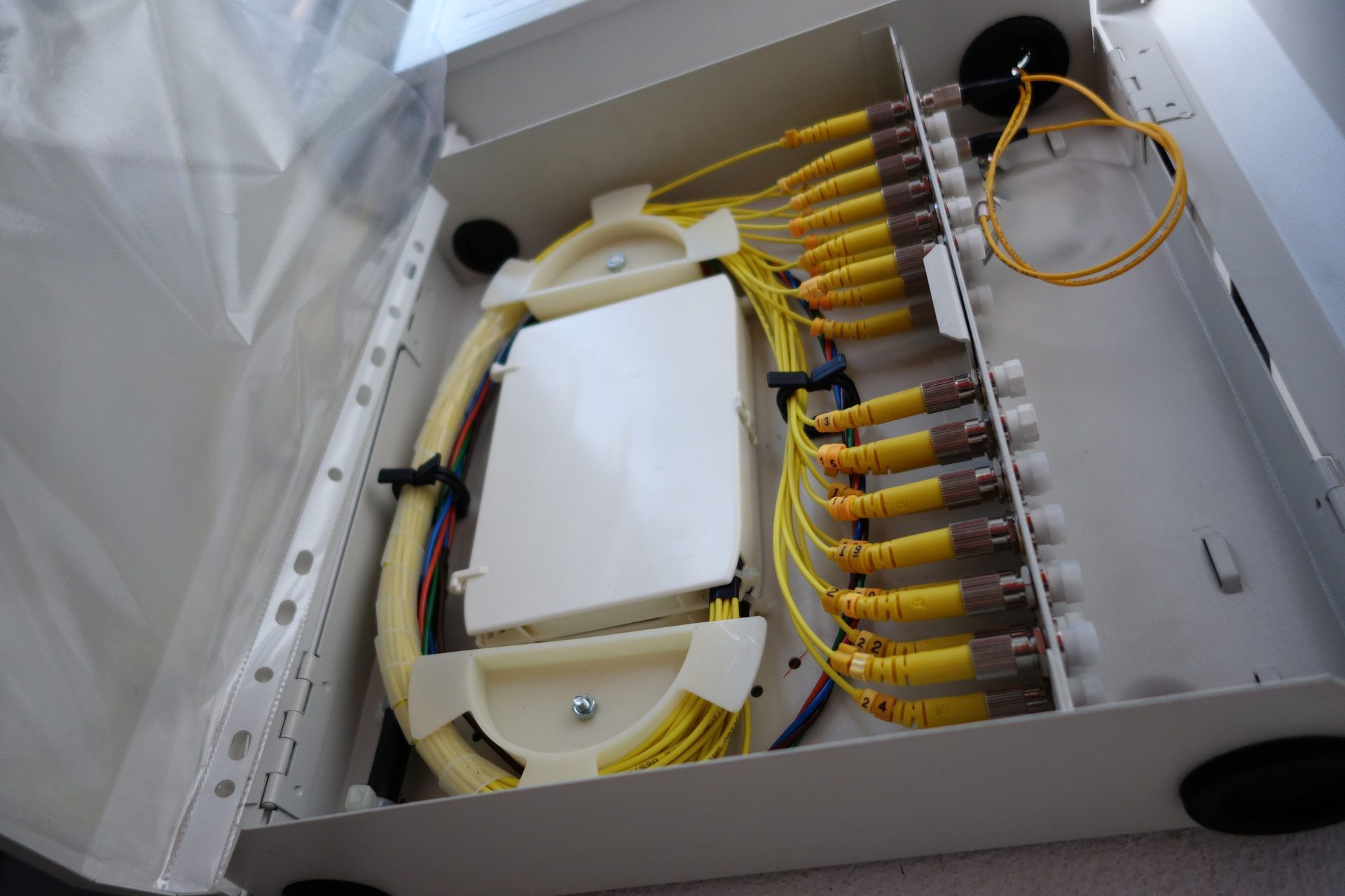 Open white metal box containing yellow fiber optic cables, connectors, and a white enclosure.