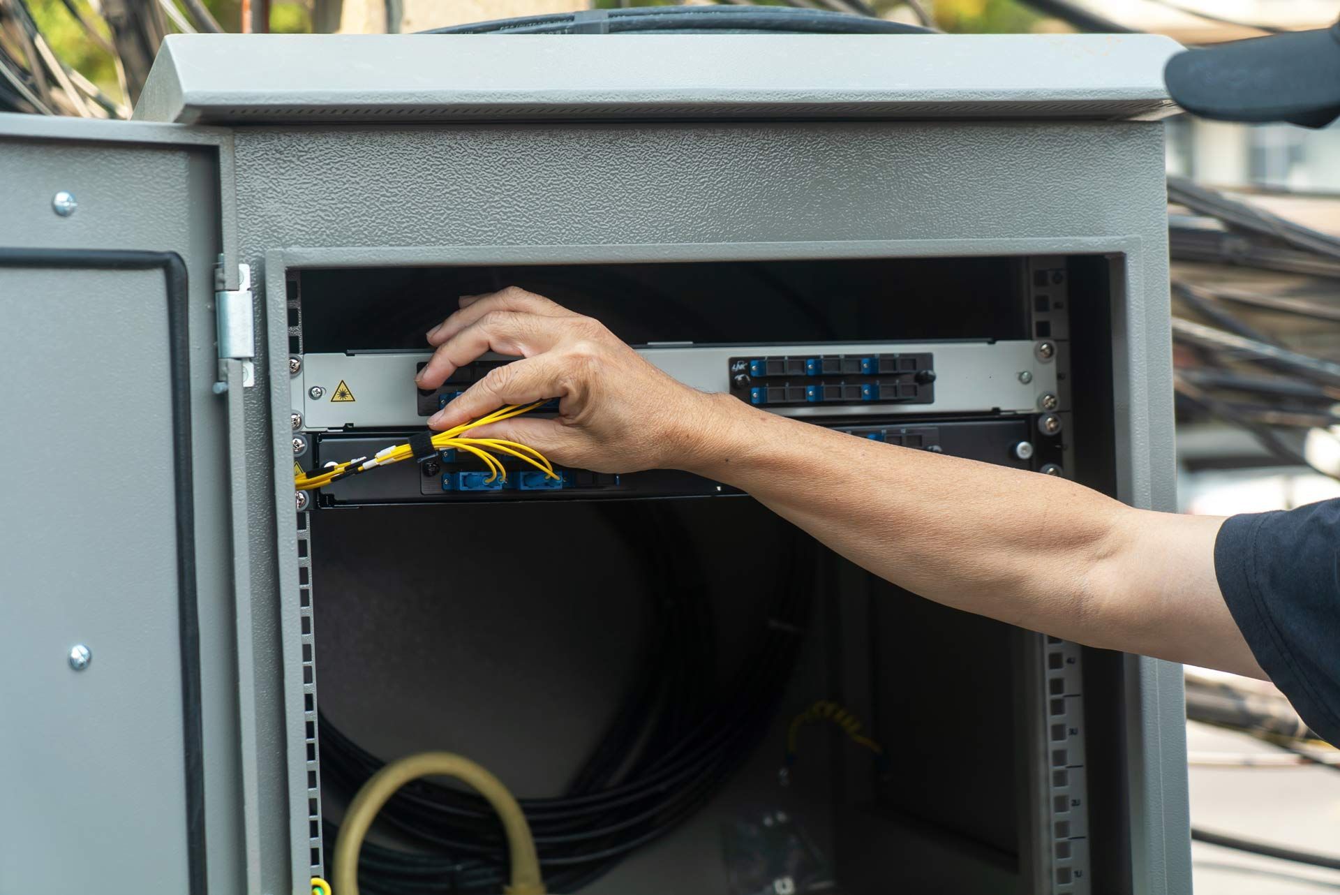 Person installing network cables in a metal cabinet outdoors.
