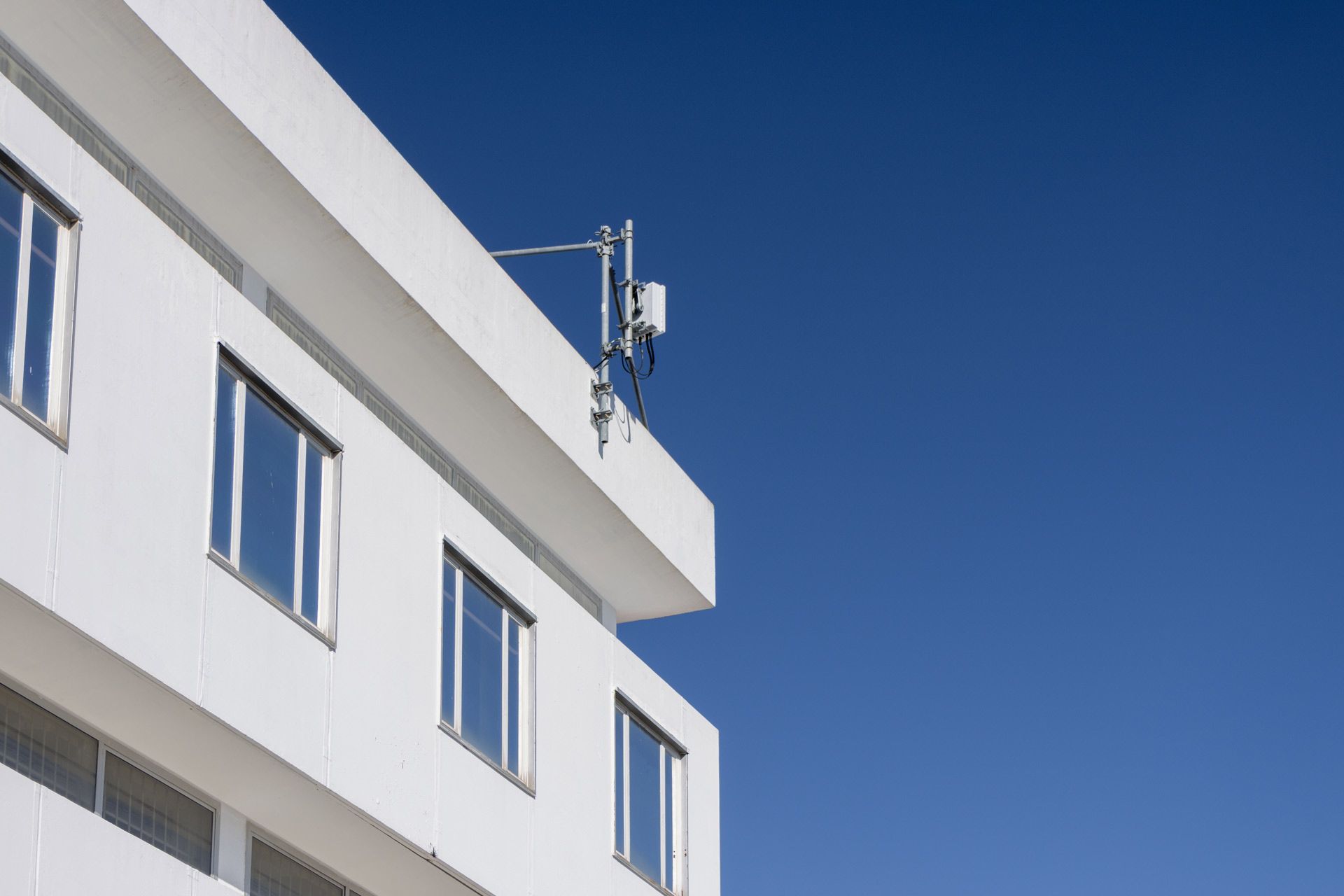 White building with square windows and a communications antenna against a clear blue sky.