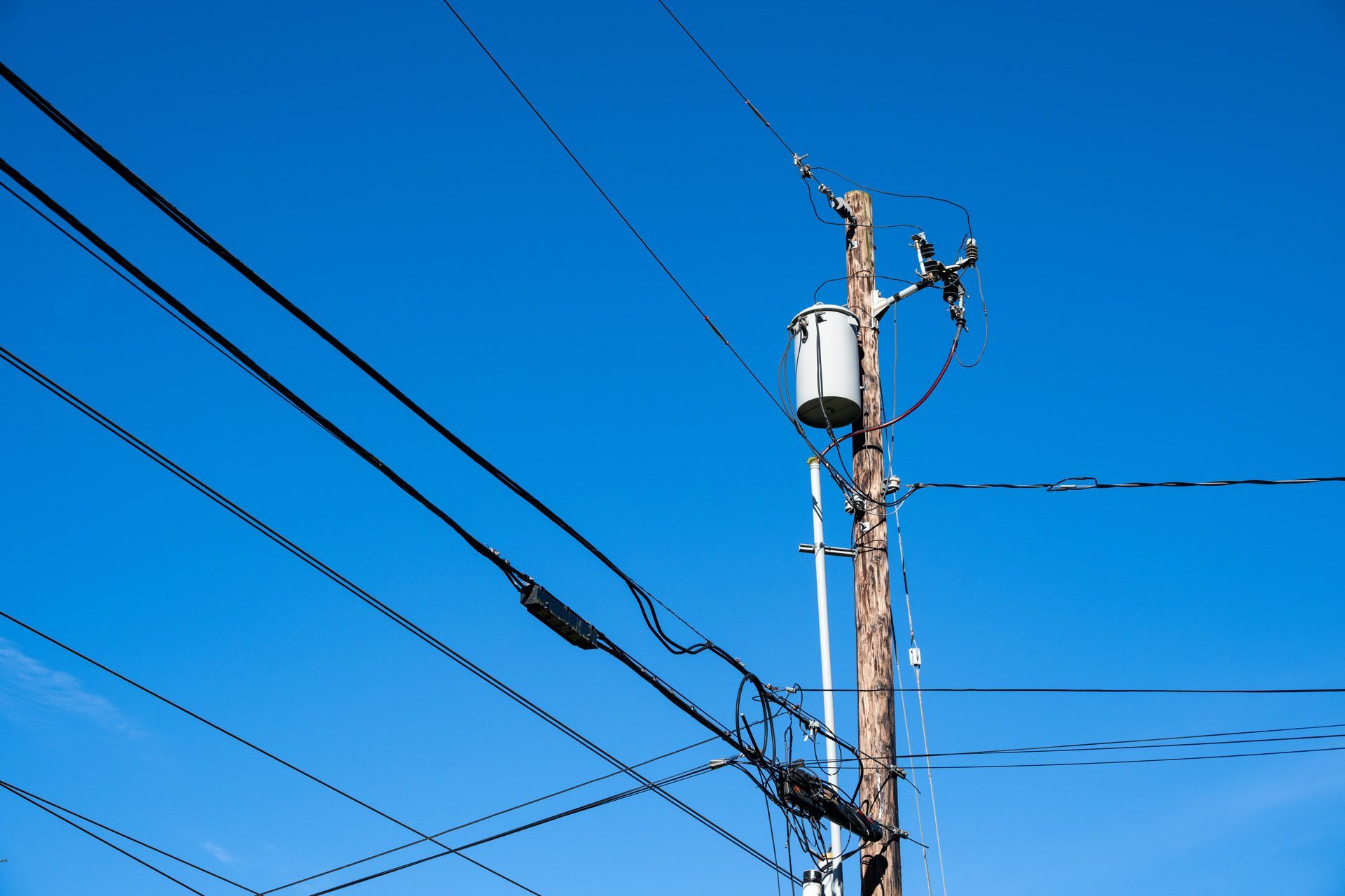 Utility pole with transformer and power lines against a clear blue sky.