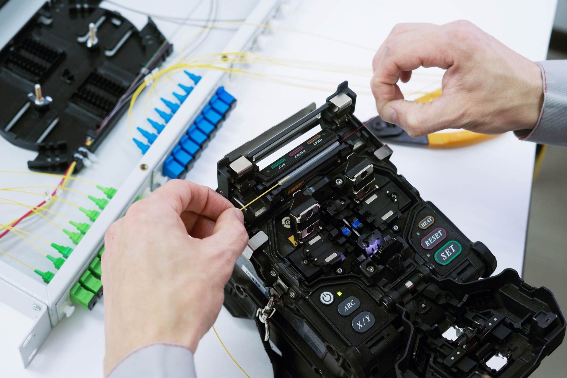 Hands working with fiber optic cables and splicing equipment.