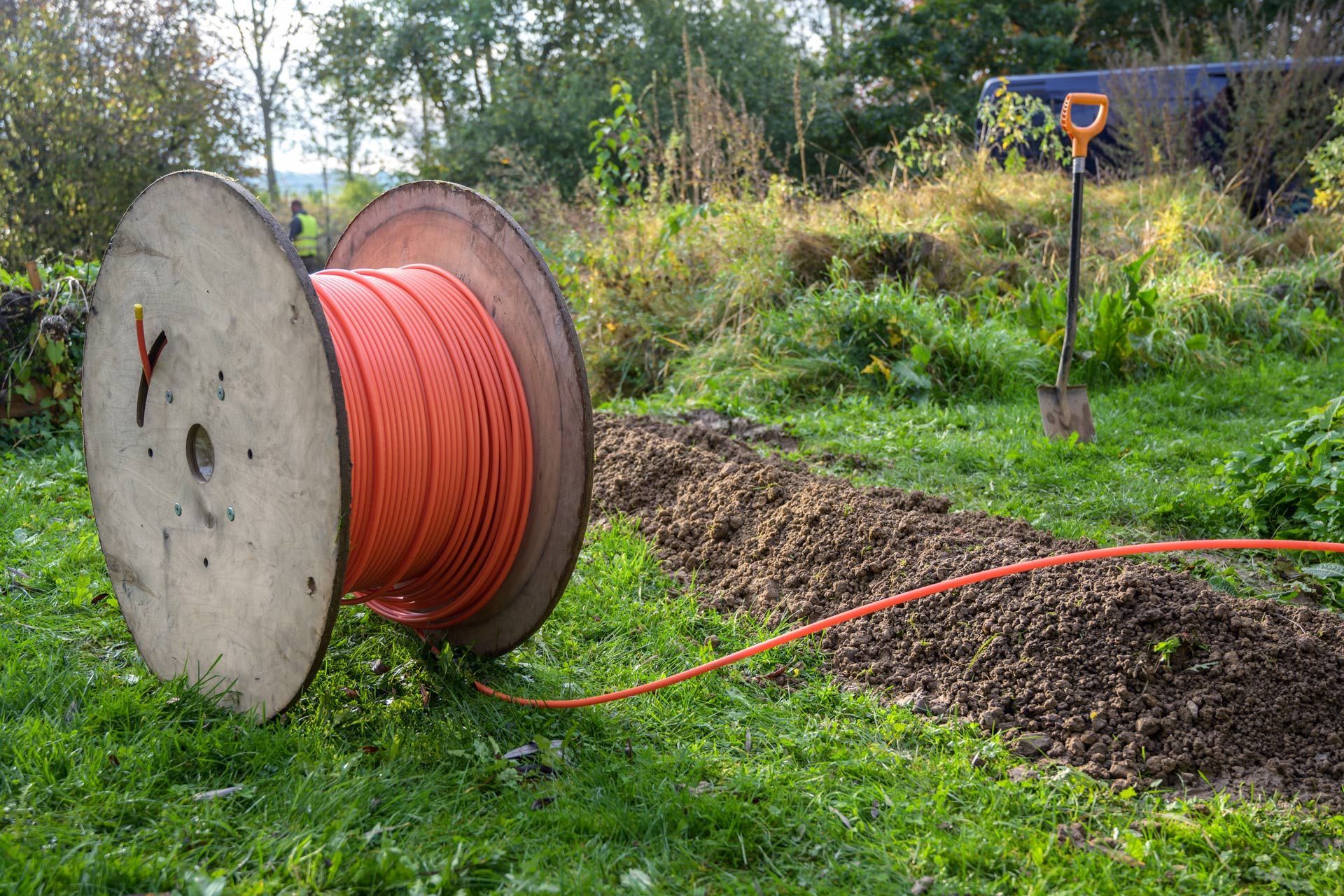 Orange cable on spool in yard, being laid in a trench. Shovel in background.