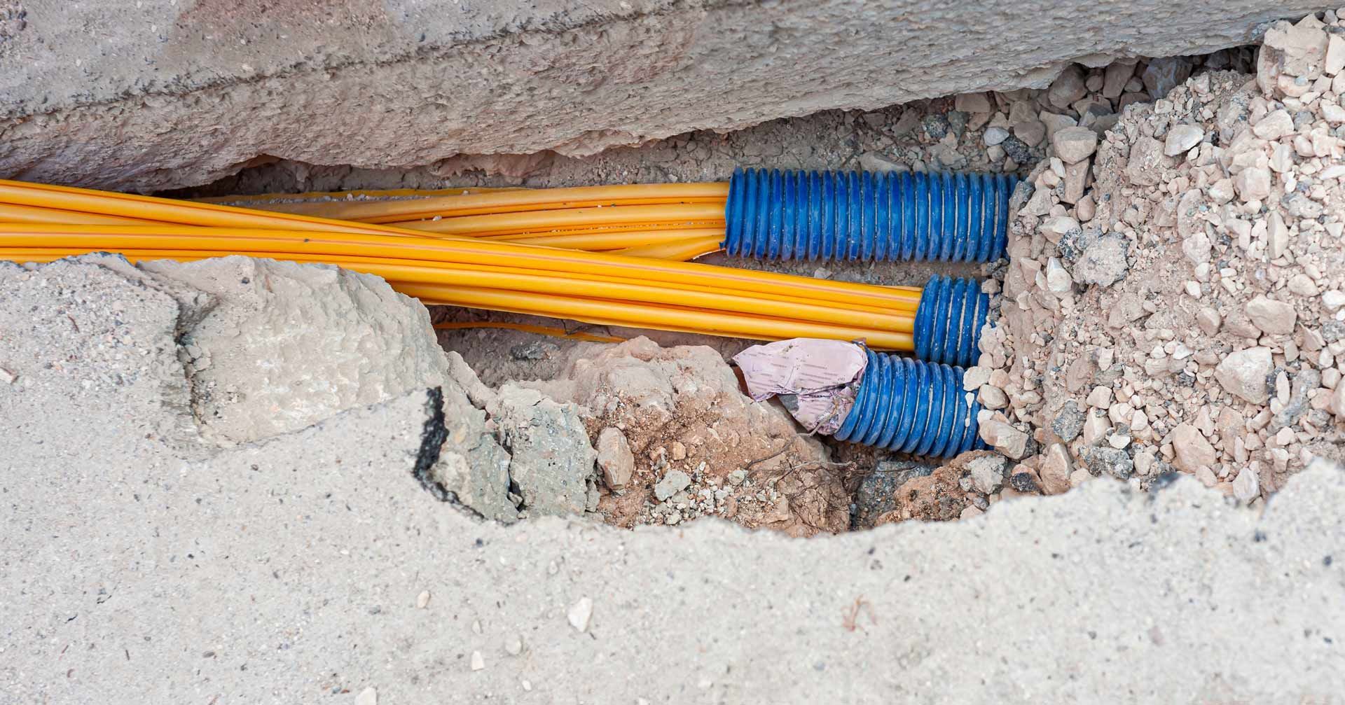 Yellow electrical conduits run through a concrete trench, bundled with blue corrugated protectors.