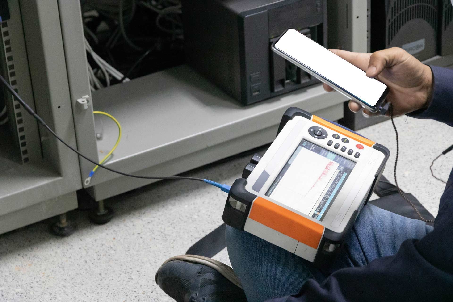 Person using a fiber optic testing device connected to a server in a data center.