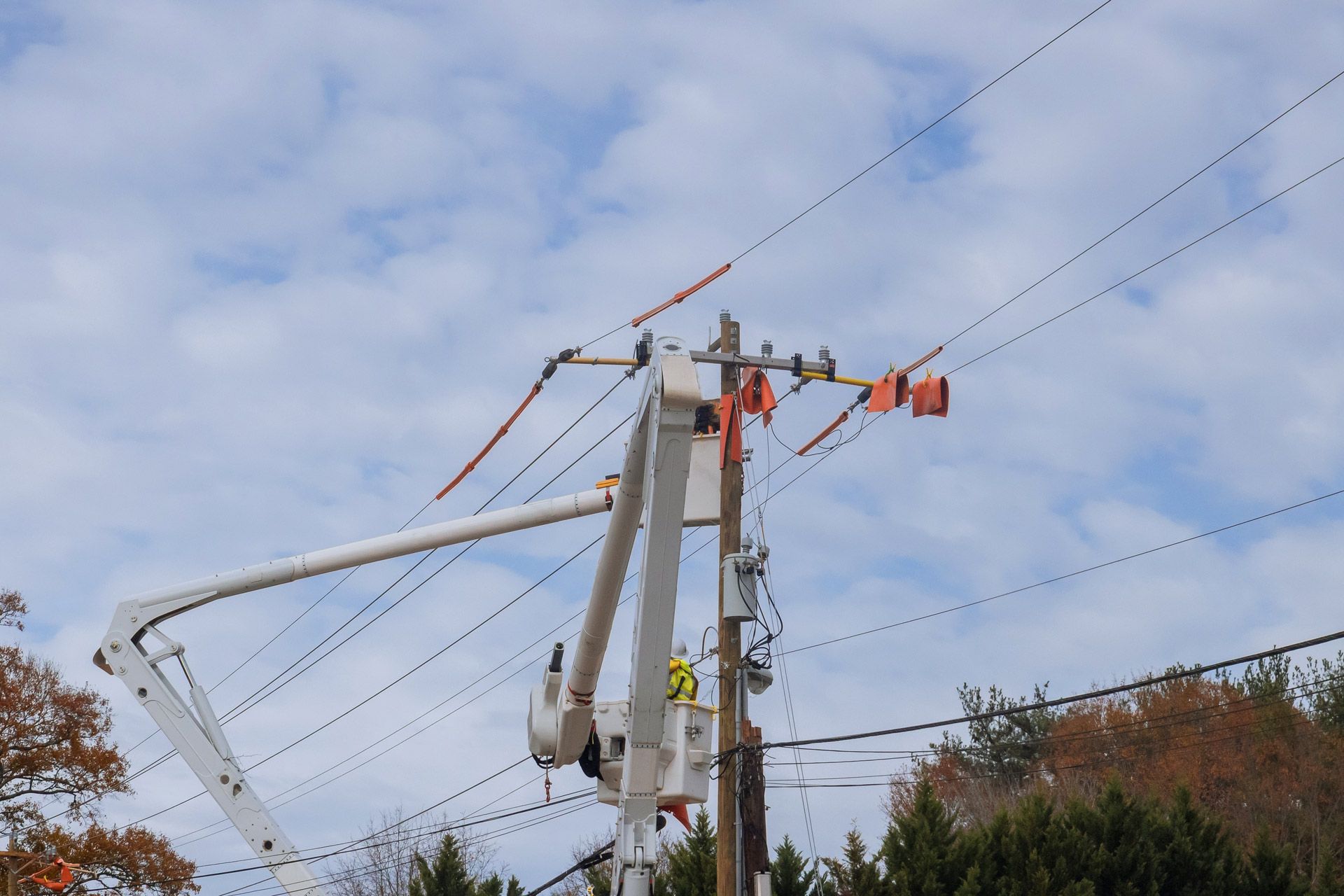 Lineworker in a bucket truck working on power lines attached to a utility pole against a cloudy sky.