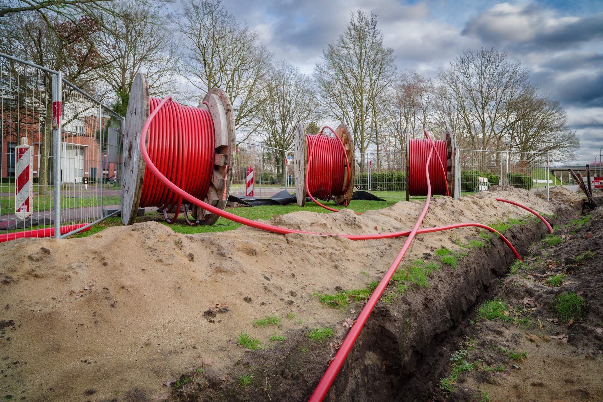 Red cables on spools, running into a trench, for underground utilities. Outdoor setting.