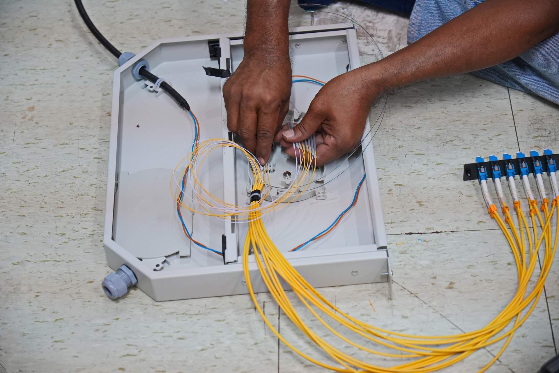 Person working with fiber optic cables inside a metal box.