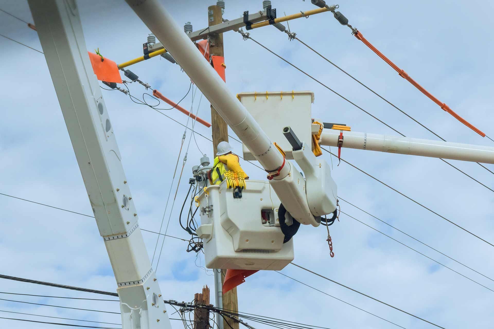 Lineman in a bucket truck working on power lines against a cloudy sky.