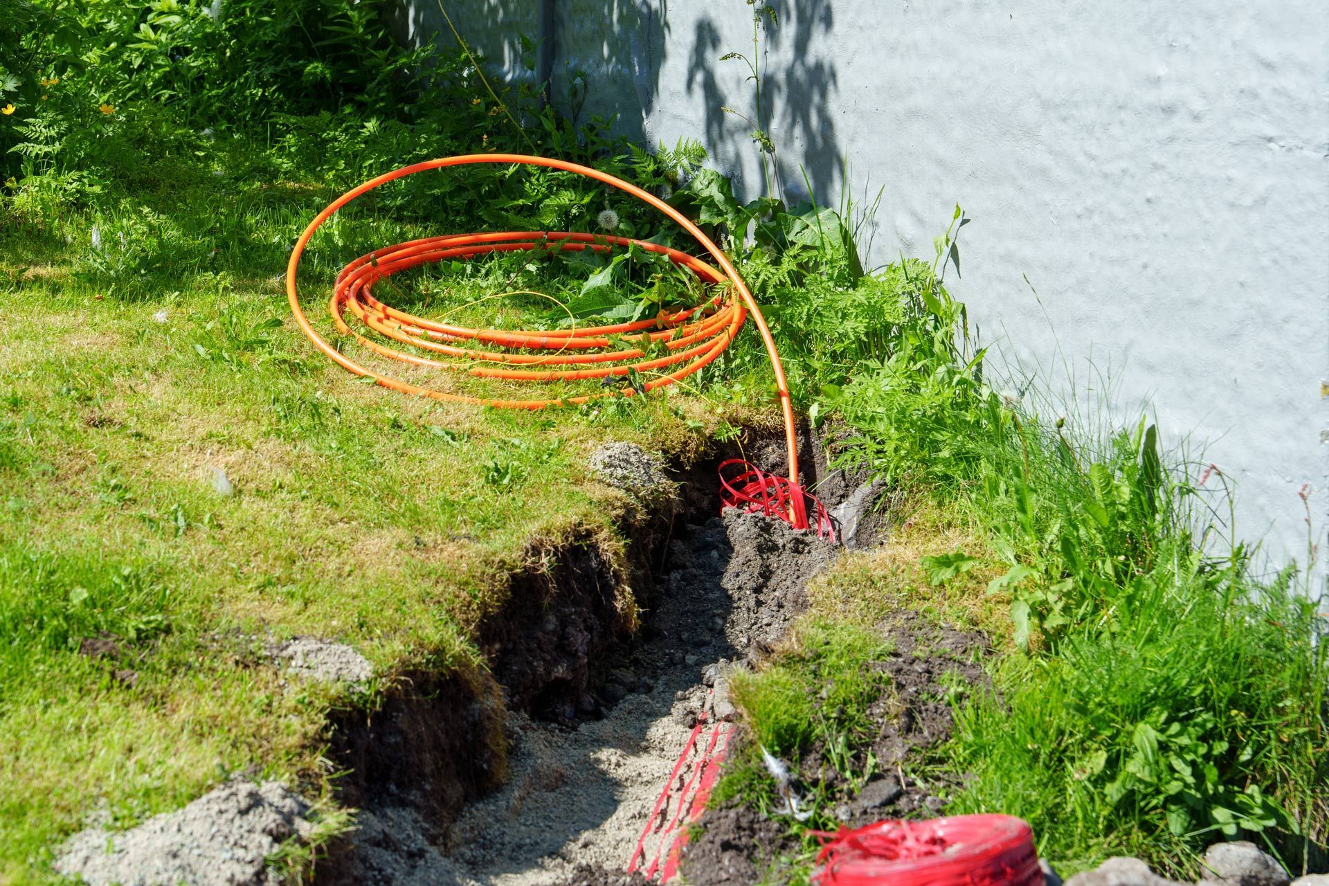 Orange cable in a trench near a grassy area and concrete wall.