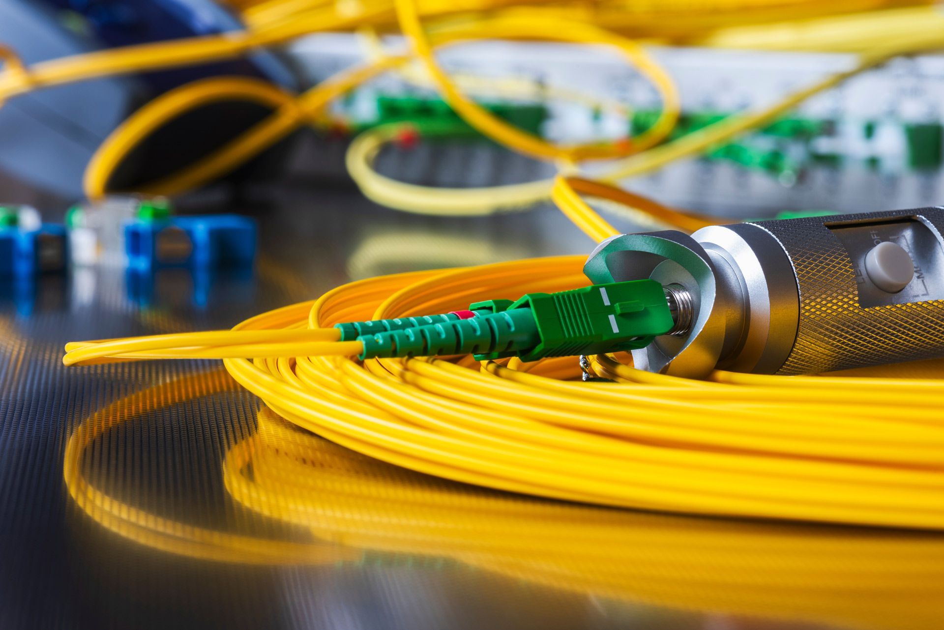 Yellow fiber optic cable with green connectors and a silver tool.